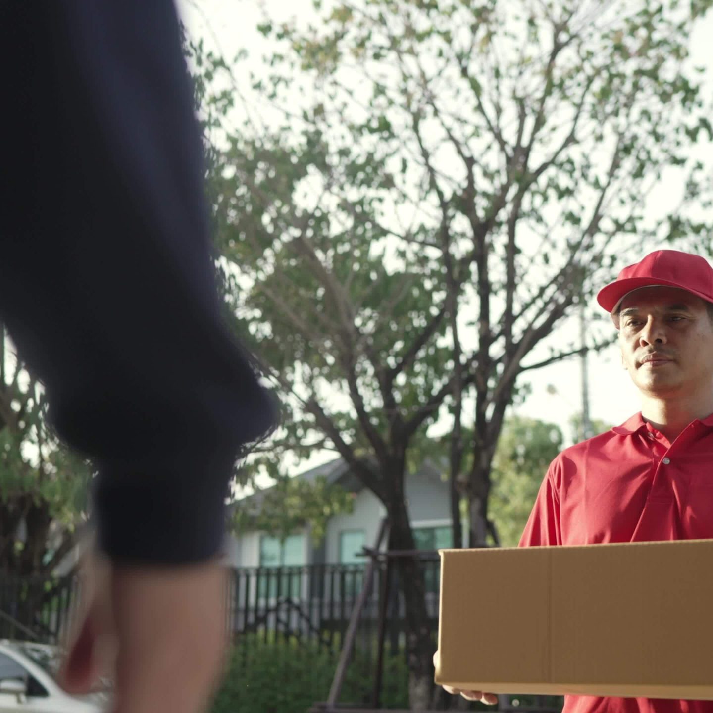 a-parcel-delivery-worker-wearing-a-red-uniform-is-holding-a-parcel-box-to-the-recipient-contact-the-receiver-in-front-of-the-house-free-video